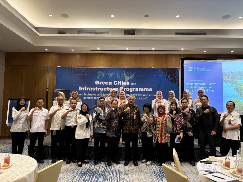 A team from the Surabaya city area stand up in conference room behind a banner of the GCIEP programme